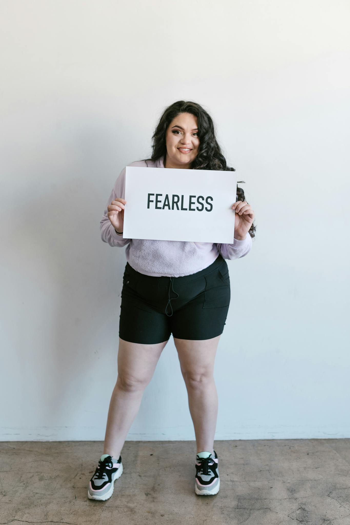 A confident woman stands proudly holding a sign that reads 'Fearless'.