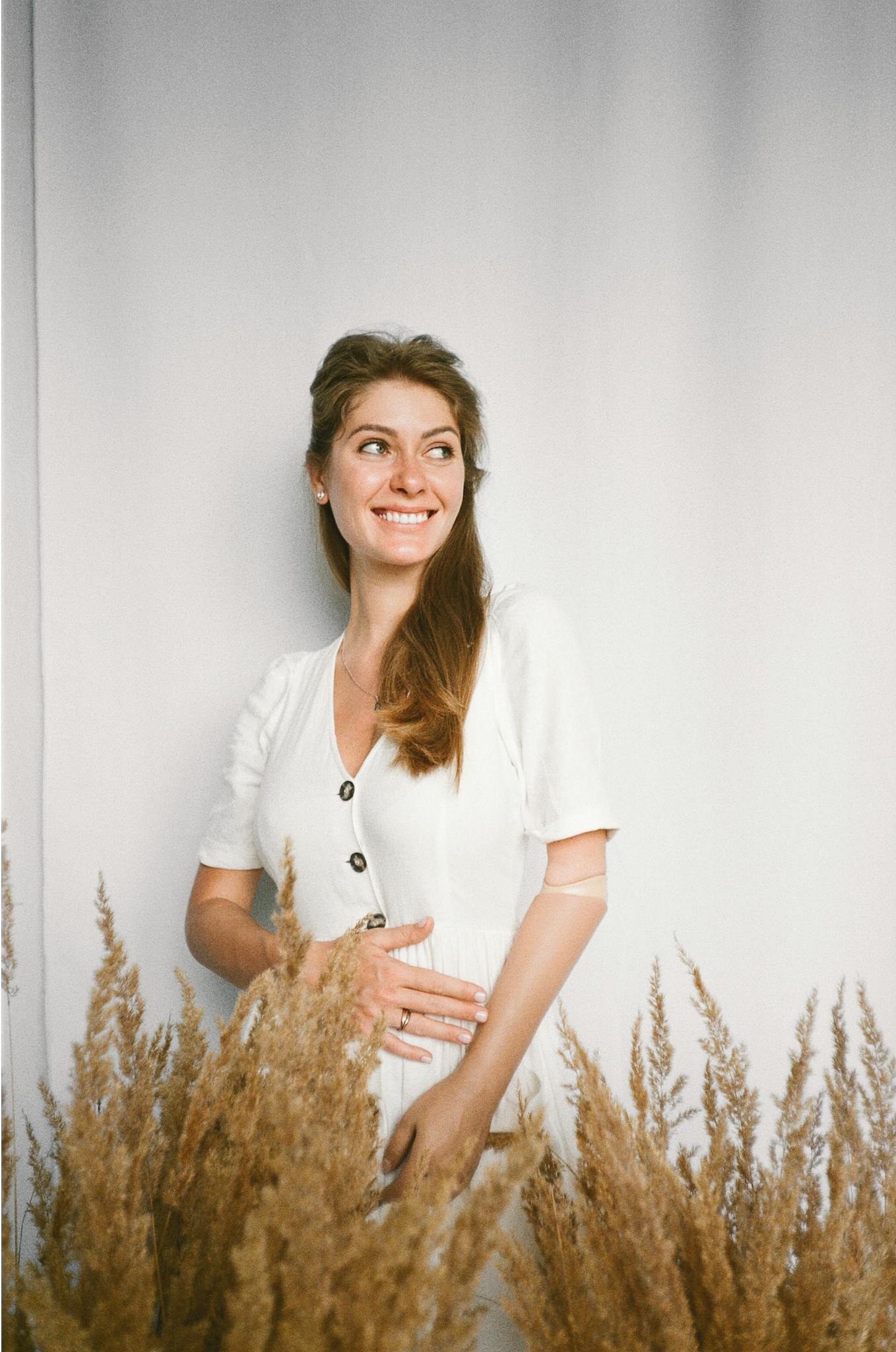 Smiling woman with prosthetic arm surrounded by dried grasses, embracing natural beauty.