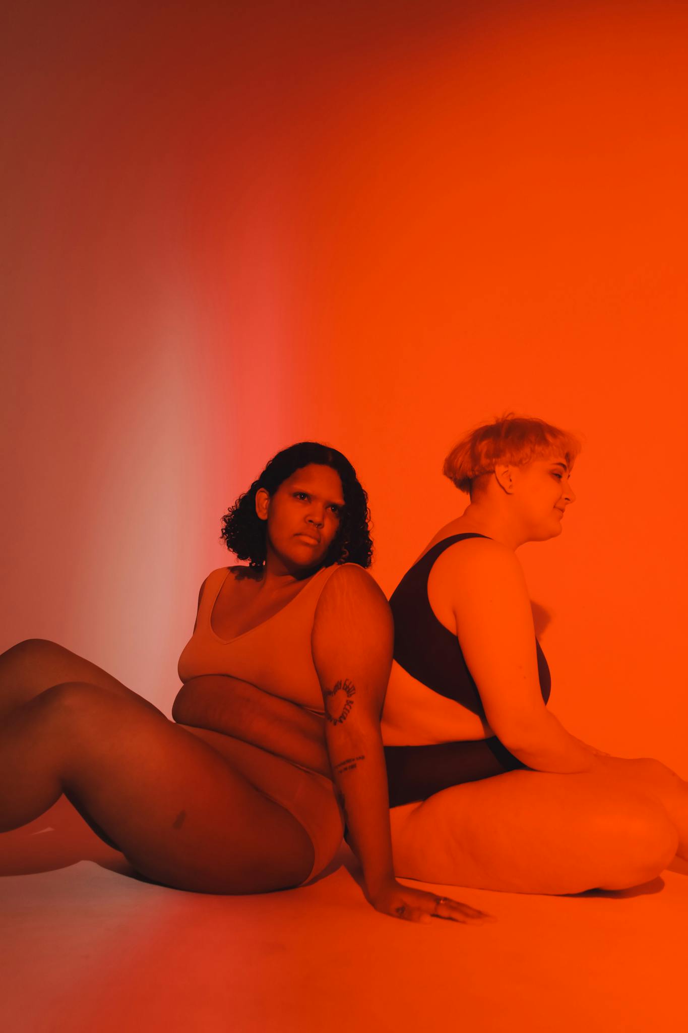 Vibrant studio portrait celebrating body positivity with two plus-size women sitting back to back.